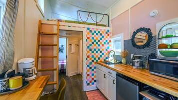 A compact kitchen with a colorful checkered backsplash, a wooden countertop, and a built-in microwave.