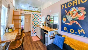 A compact kitchen with a colorful checkered backsplash, a wooden dining table, and a black sofa with a blue cushion. - The Florio, Tiny Home, River, Hiking, and Rafting! (Sylva)