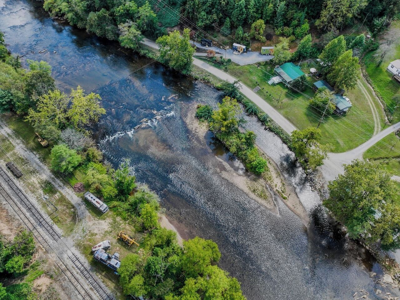 Vue aérienne d’une propriété située au bord de la rivière, avec une route, un petit bâtiment et un champ verdoyant.