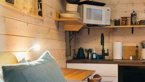 A cozy kitchen with wooden walls, a microwave, a sink, and various kitchen utensils.