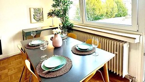 Egy étkező, ahol egy négy személyes asztal van megterítve, egy radiátor és egy ablak, melyből zöld tájra nyílik kilátás.