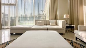 A modern hotel room with a large bed, a sofa, a chair, and a view of a cityscape through large windows. - Panoramic Burj Khalifa View Luxury Penthouse 1BR (Dubai)