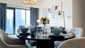 A dining area with a round table set for four, a chandelier, and a city view through large windows. - Stunning Burj View Sky High Luxury 2BR (Dubai)