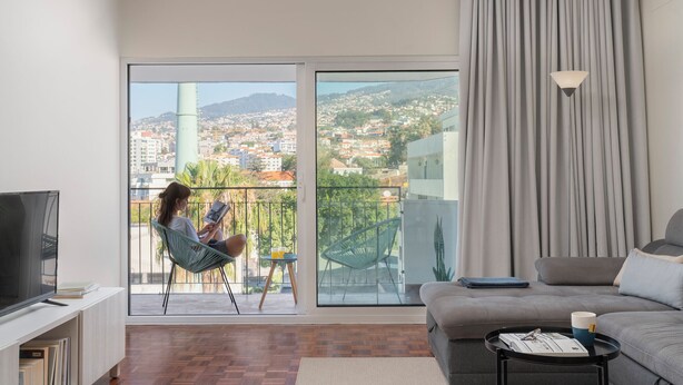 Una sala de estar moderna con un amplio ventanal corredero que da a un balcón, un televisor de pantalla plana, un sofá y una pequeña mesa de centro.