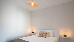 Una cama bien hecha con un edredón verde, dos mesitas de noche con velas y una lámpara colgante.