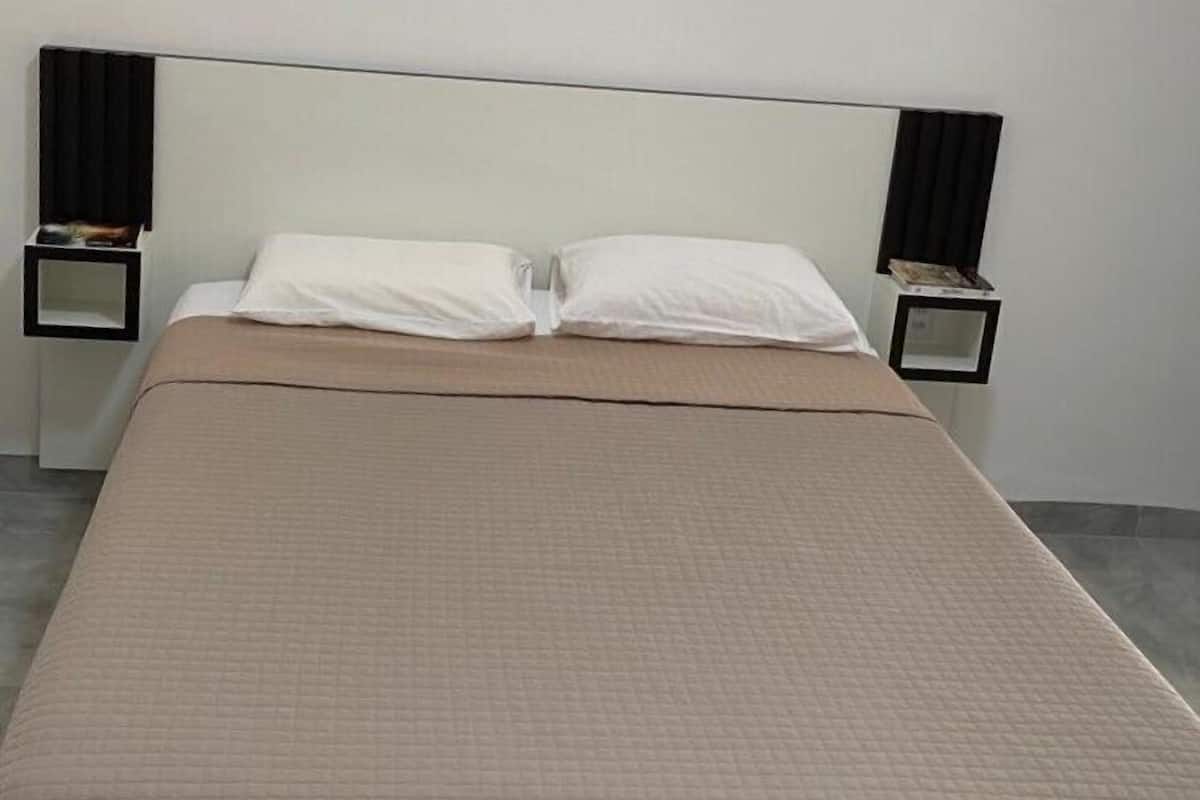 A bed with a beige quilted bedspread, two white pillows, and two bedside tables with black lamps.