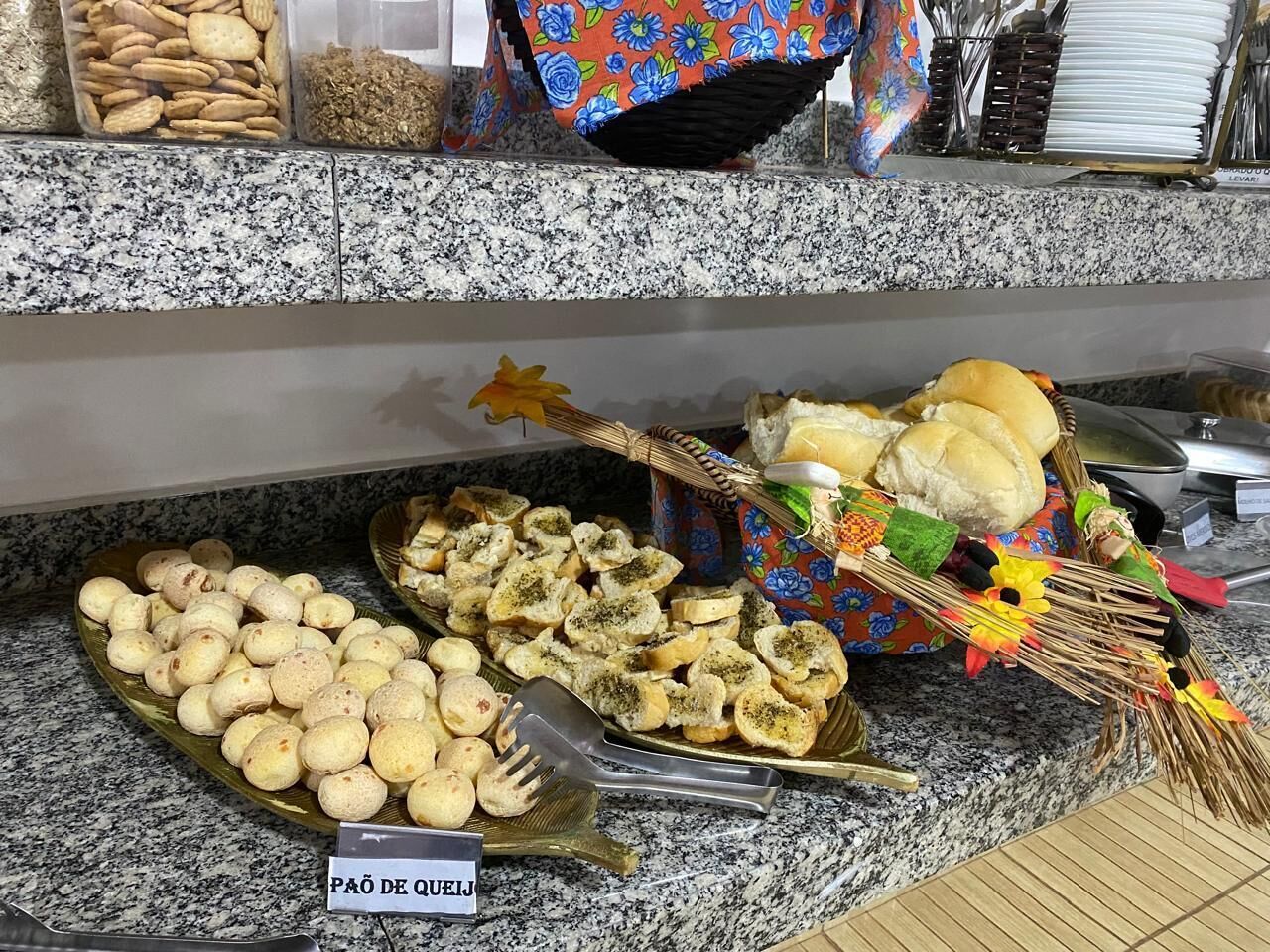 Un buffet proposant divers aliments, notamment du pain, des crackers, et une pancarte indiquant « PAO DE QUEIJ ».