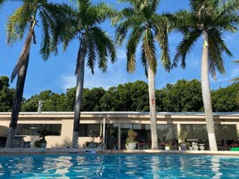 Un área de piscina con palmeras, un edificio con tejado de azulejos y un cielo azul despejado.