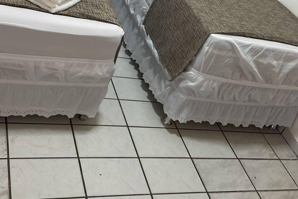 Two single beds with white linens and brown blankets, a white pillow, and a tiled floor.