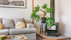 Un salon avec un canapé, un tableau encadré, une grande plante, une cheminée et une petite table.