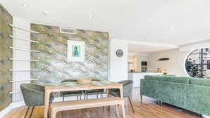 Un salon moderne comprenant un coin repas, un canapé vert, un parquet en bois et un mur orné d’une fresque sur le thème de la nature.