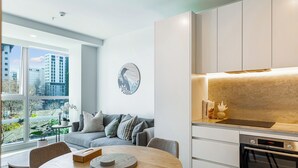 A modern kitchen with a built-in oven, a dining area with a round table, and a view of the city through large windows. - Chic Central Apt with Gym and Pool by Zodiak Stays (Auckland)