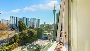 A cityscape with modern high-rise buildings, a prominent tower, and a view through a window with blinds. - Chic Central Apt with Gym and Pool by Zodiak Stays (Auckland)