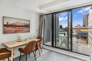 A modern room with a dining table, chairs, a large window with a city view, and a framed landscape painting on the wall.