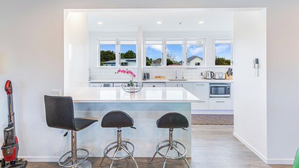 A modern kitchen with a large island, bar stools, and a view of the neighborhood. - Ellerslie 3BR House | Fresh Reno | Zodiak Stays (Auckland)