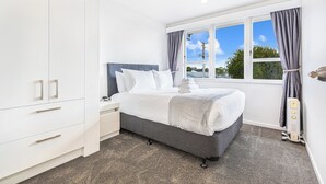 A modern bedroom with a large bed, white wardrobe, and a window with curtains. - Ellerslie 3BR House | Fresh Reno | Zodiak Stays (Auckland)
