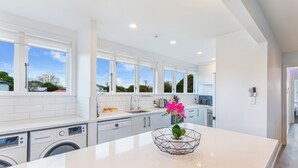 A modern kitchen with white cabinetry, a central island, and a view of the outdoors. - Ellerslie 3BR House | Fresh Reno | Zodiak Stays (Auckland)