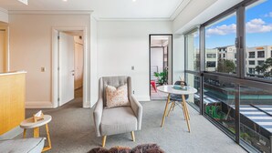 A modern hotel room with a grey armchair, a small round table, and a view of the city through large windows. - Viaduct Harbour Views w/ Free Parking-Zodiak Stays (Auckland)