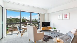 A modern living room with a large window, a sofa, a coffee table, and a TV. - Viaduct Harbour Views w/ Free Parking-Zodiak Stays (Auckland)