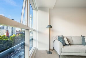 A modern living room with a large window, a floor lamp, and a sofa with cushions. - Modern Bright Central Apartment by Zodiak Stays (Auckland)
