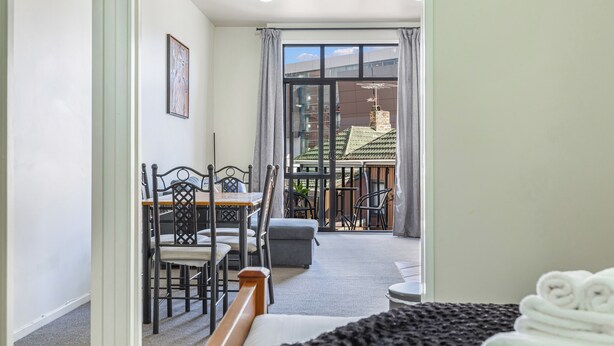 A hotel room with a balcony, a dining area with a table and chairs, and a bed with a neatly made bed. - 1BR Grey Lynn Haven+Parking, Balcony Zodiak Stays (Auckland)