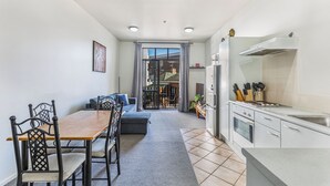 A modern kitchen with a dining area, featuring a wooden table, chairs, and a sofa. - 1BR Grey Lynn Haven+Parking, Balcony Zodiak Stays (Auckland)