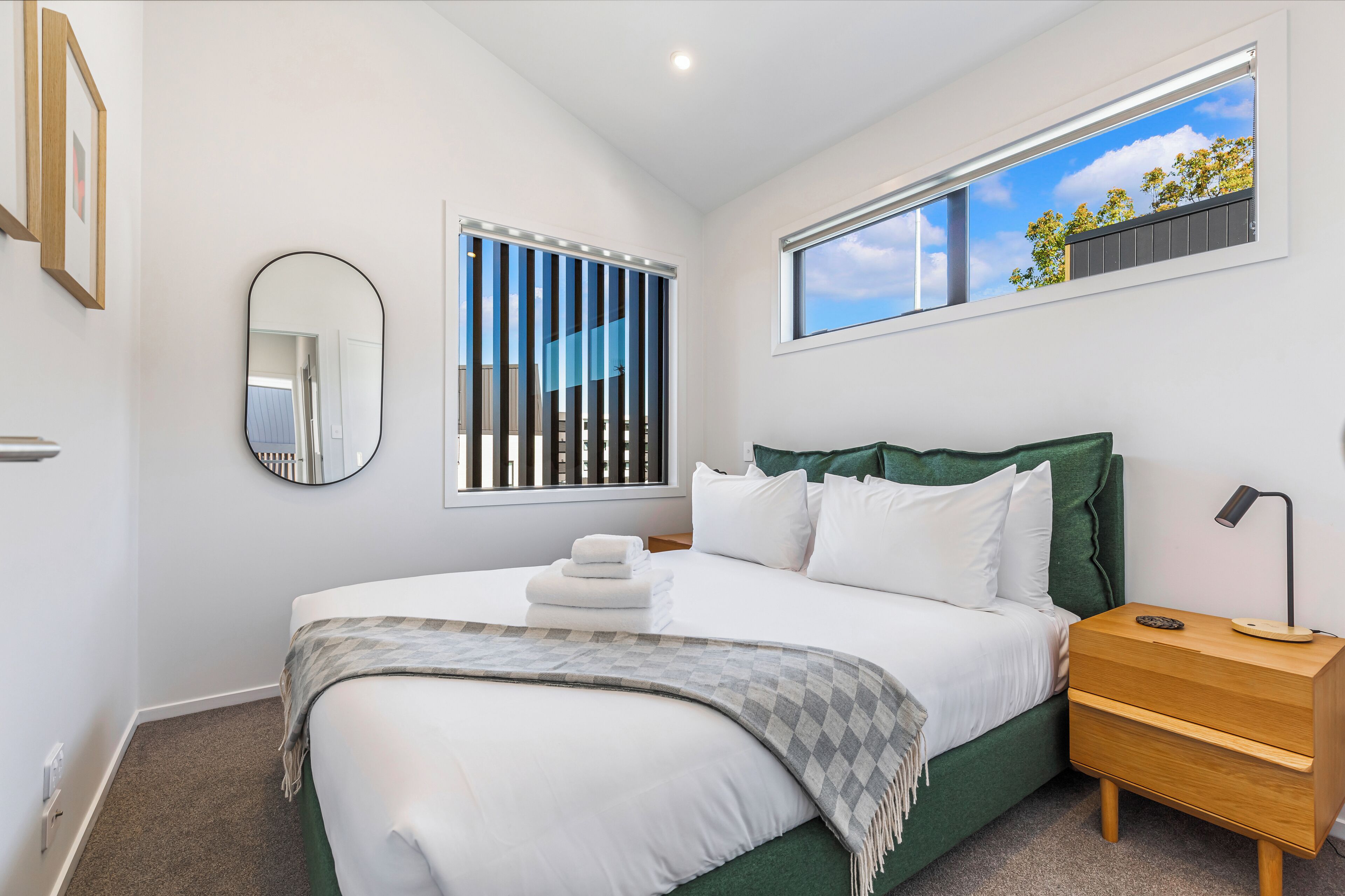 A bedroom with a large bed, a nightstand, a mirror, and a window with a view of trees.