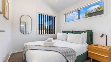 A bedroom with a large bed, a nightstand, a mirror, and a window with a view of trees.