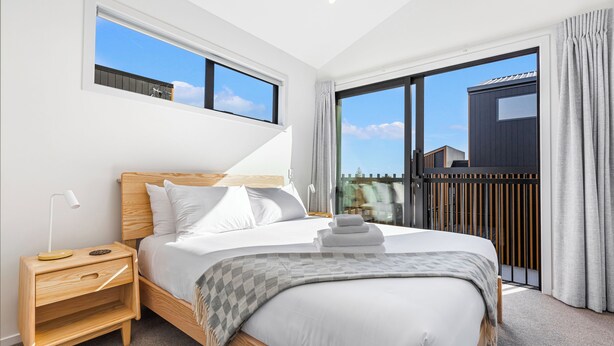 A modern bedroom with a large bed, a nightstand, a window, and a view of the outside.