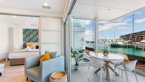 Une chambre d’hôtel moderne dotée d’un balcon, d’un lit, d’un coin salon et offrant une vue sur les bateaux et les bâtiments.