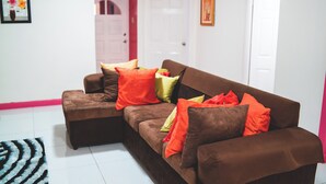 Ein braunes Sofa mit mehreren bunten Kissen, einem gemusterten Teppich und einer weißen Tür im Hintergrund.