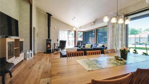 Amplia sala de estar con una gran mesa de madera para comer, asientos cómodos, chimenea y ventanas amplias que ofrecen vistas al exterior.