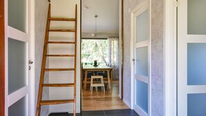 Un pasillo con una escalera de madera, un comedor con mesa y sillas, y vistas al exterior.