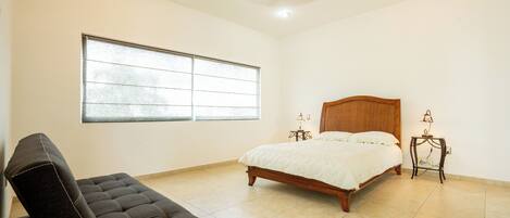 Un dormitorio con cama, una silla, un ventanal y un ventilador de techo.