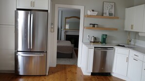 A compact kitchen with white cabinets, a stainless steel refrigerator, a dishwasher, and a small countertop with a sink and shelves. - Charming renovated 1-bedroom in downtown Biddeford (Biddeford)
