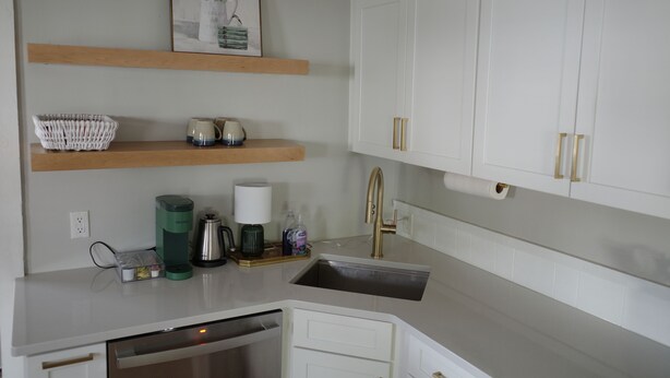 A kitchen with white cabinets, a stainless steel sink, and a wooden shelf above. - Charming renovated 1-bedroom in downtown Biddeford (Biddeford)
