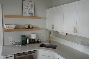 A kitchen with white cabinets, a stainless steel sink, and a wooden shelf above. - Charming renovated 1-bedroom in downtown Biddeford (Biddeford)