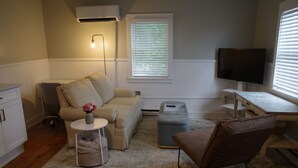 A living room with a sofa, ottoman, side table, and a television. - Charming renovated 1-bedroom in downtown Biddeford (Biddeford)