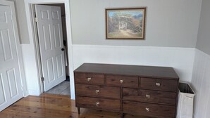 A wooden dresser with drawers, a white trash bin, and a door leading to another room. - Charming renovated 1-bedroom in downtown Biddeford (Biddeford)