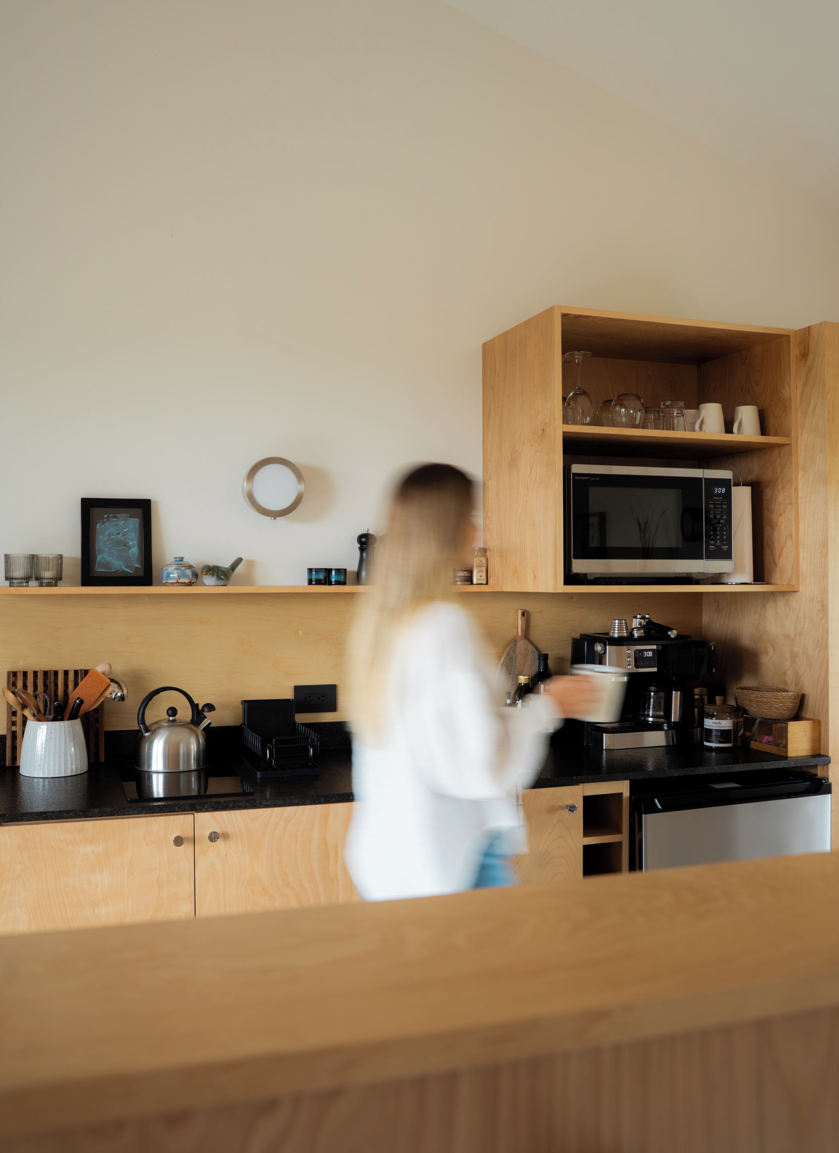 Een moderne keuken met houten kastjes, een magnetron, een waterkoker en diverse keukengerei.