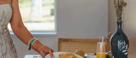 A breakfast table with croissants, a bowl of fruit, and a glass of orange juice.