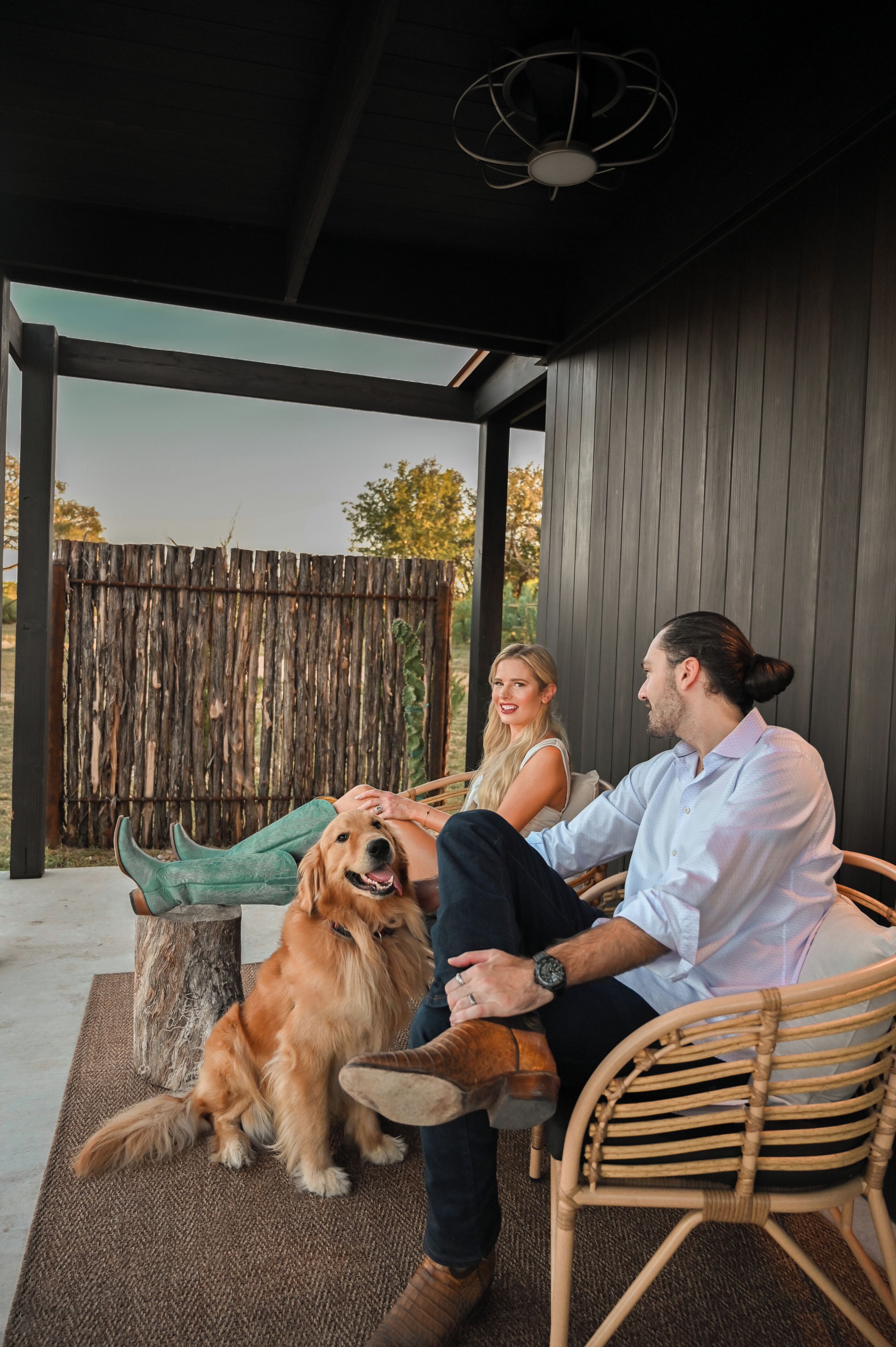 A covered outdoor seating area with a wooden fence, a dog, and two people.