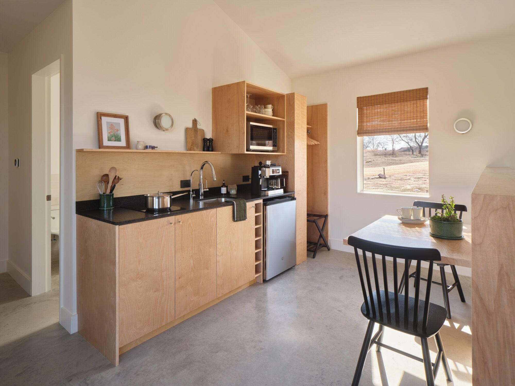A compact kitchen with wooden cabinets, a black countertop, a sink, a coffee maker, and a window with a view of the outdoors.