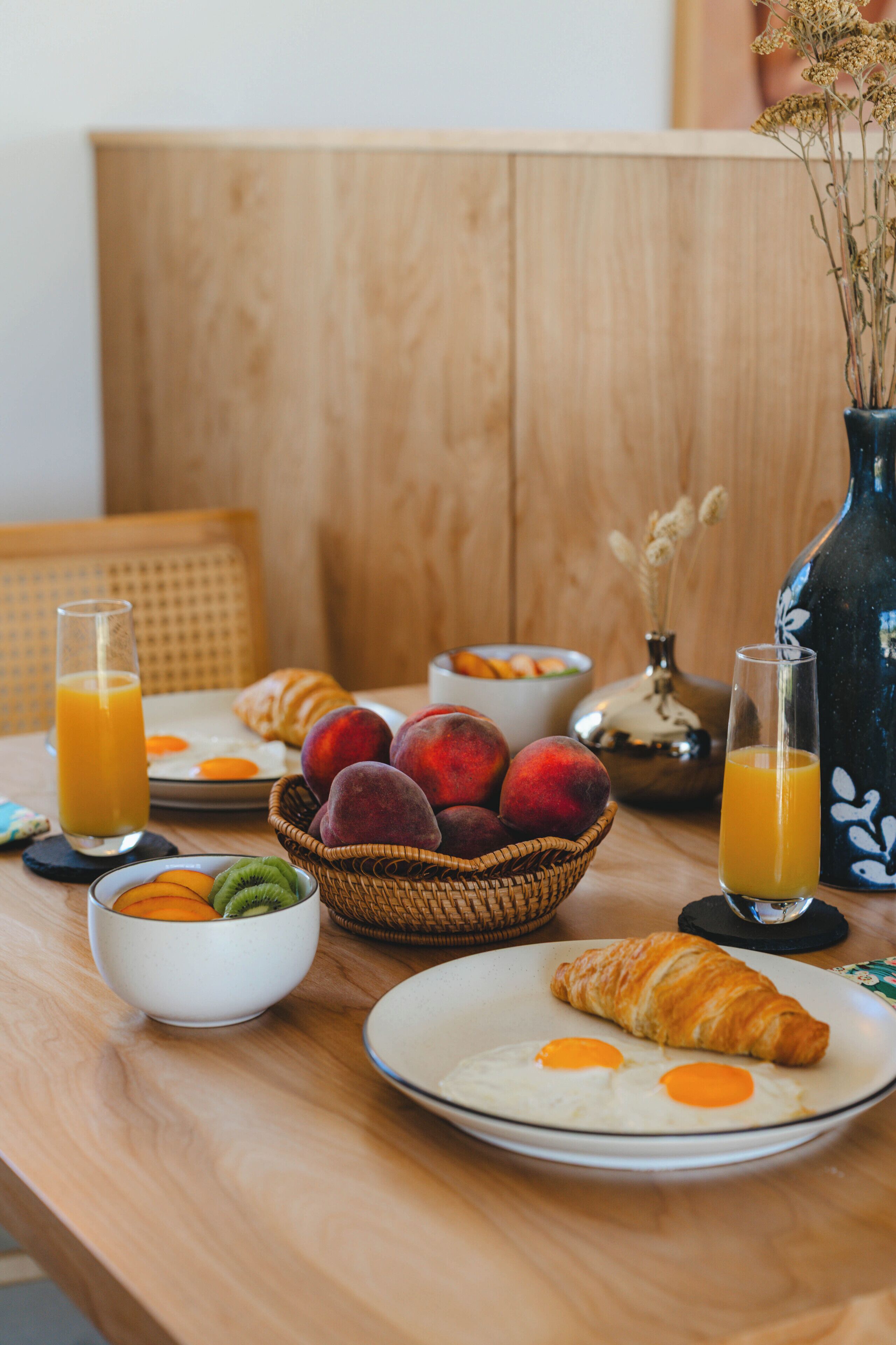 A breakfast table with plates of eggs, croissants, and a basket of fruits.