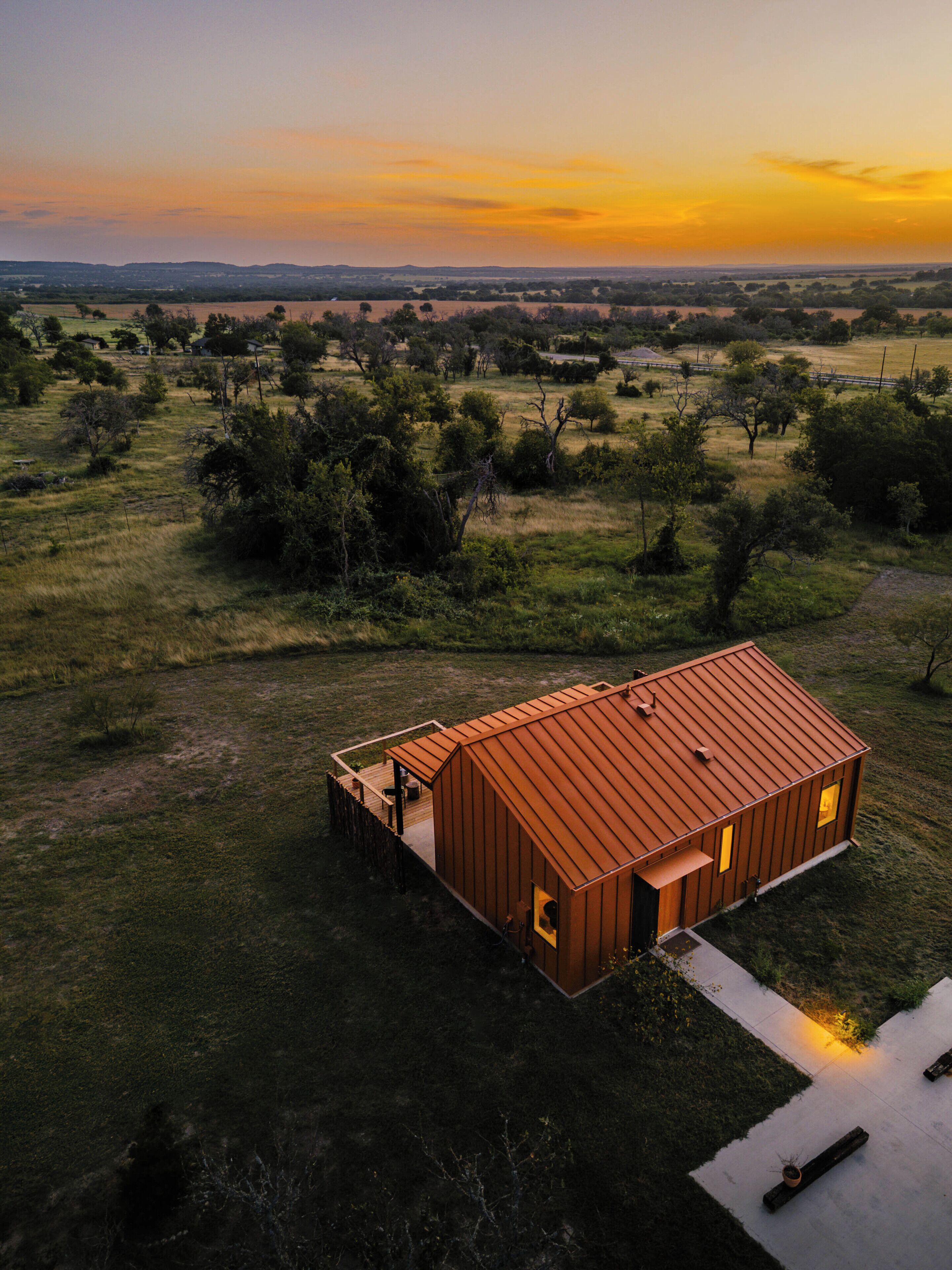 A single-story metal building with a flat roof, surrounded by a grassy field and trees, during sunset.