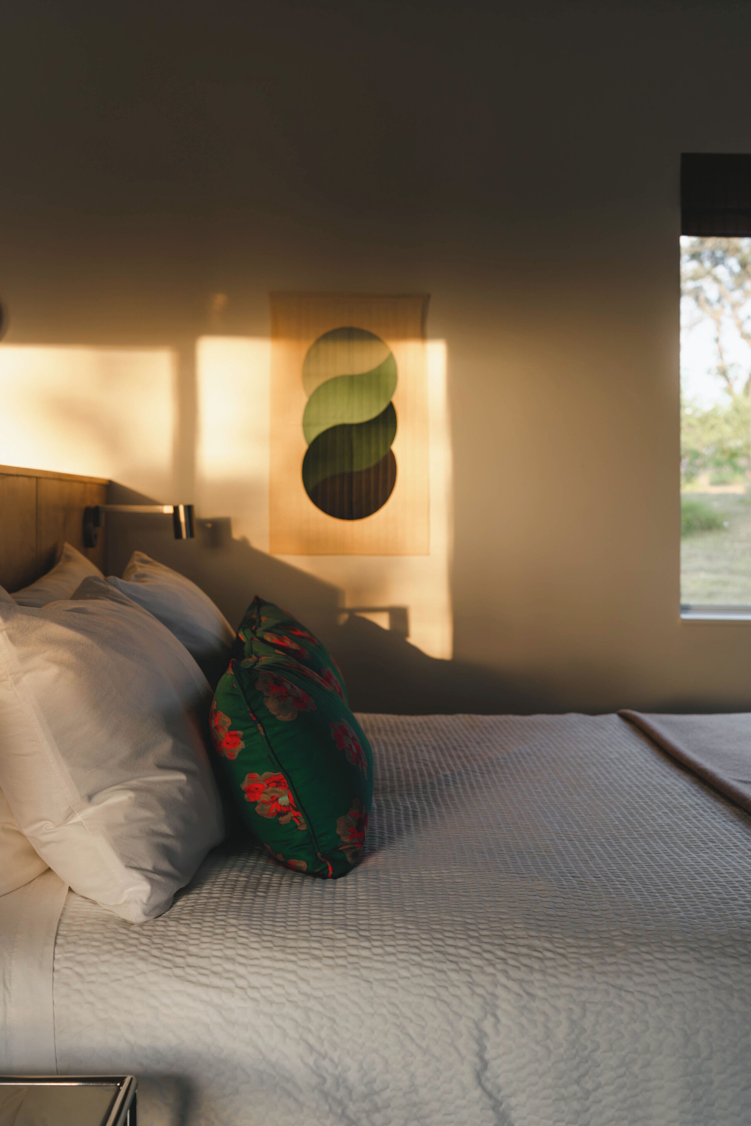 Un dormitorio con cama, almohadas, una lámpara de pared y una ventana.