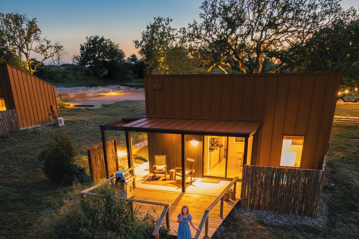 Ein moderner Außenbereich mit Feuerstelle, Sitzgelegenheiten und einer Holzterrasse, die zu einem Haus führt.