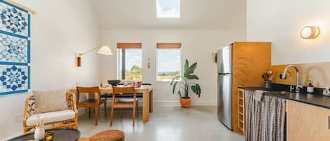 Una cocina compacta con comedor, una mesa redonda negra, un taburete de mimbre, una planta en maceta y un tragaluz.