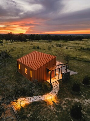 Eine moderne, eingeschossige Holzhütte mit einem steinernen Weg, der zum Eingang führt, umgeben von einer grünen Landschaft.