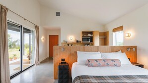 A bedroom with a bed, a bedside table, a nightstand, a wooden headboard, a built-in kitchen area, and a sliding glass door leading to an outdoor area. - The Martinsburg (Stonewall)